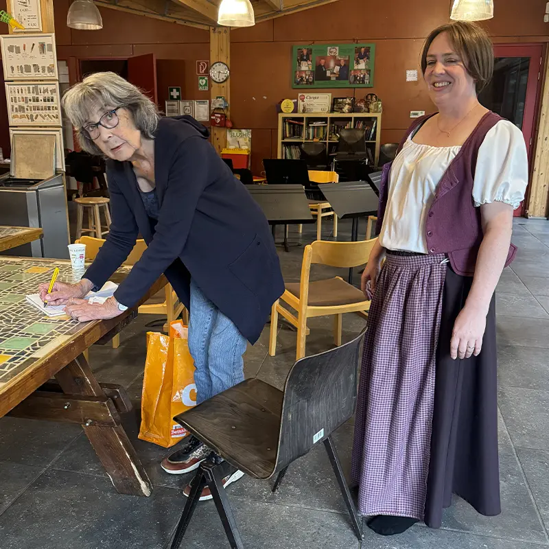 Een vrouw in kostuum naast een vrouw die aan tafel schrijft